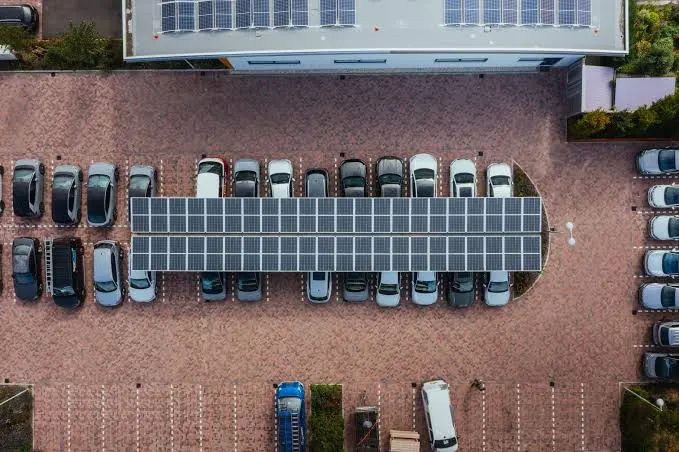 Luchtfoto van een parkeerterrein met een solar carport boven een rij geparkeerde auto's