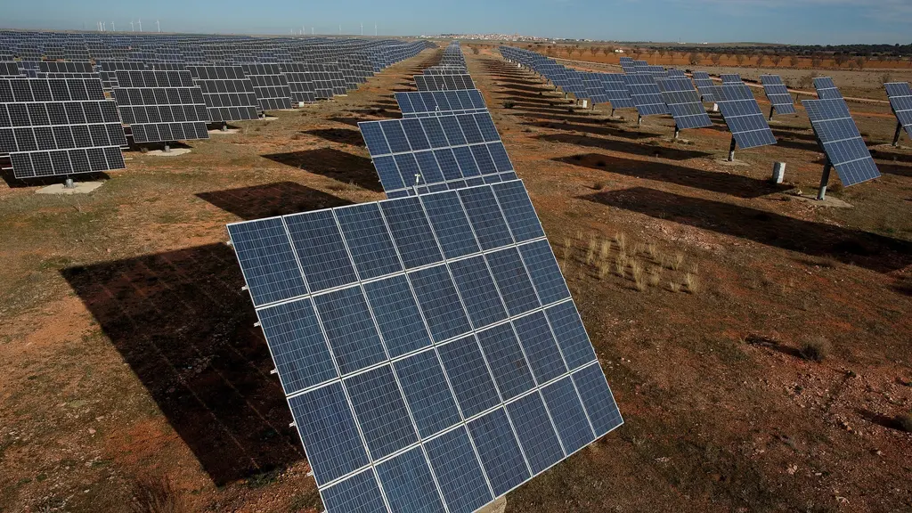 Zonnepark met rijen panelen op trackers en windturbines aan de horizon